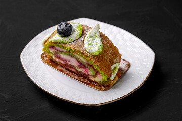 Pistachio roll decorated with blueberries lies on a saucer.