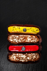 Multicolored glazed eclairs decorated with blueberries lie on a black slate plate.
