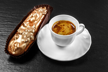 Multicolored glazed eclairs decorated with blueberries lie on a slate plate with a cup of coffee.