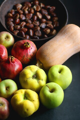 Pan with chestnuts, butternut squash and various fruit on dark background. Selective focus.