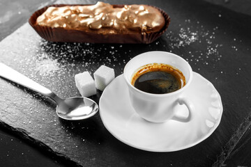 Multicolored glazed eclairs decorated with blueberries lie on a slate plate with a cup of coffee.