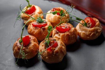Profiteroles stuffed with mushrooms and meat, decorated with herbs and tomatoes.