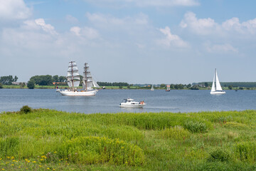 A tranquil scene over the waters by Tiengemeten, where a grand tall ship sails gracefully, flanked...