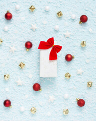 Christmas composition. Snow on a blue pastel background with gift box in the middle. White, red and golden decorations. Winter, new year concept. Card and advent minimal creative concept.