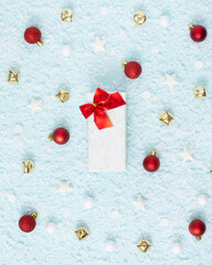 Christmas composition. Snow on a blue pastel background with gift box in the middle. White, red and golden decorations. Winter, new year concept. Card and advent minimal creative concept.