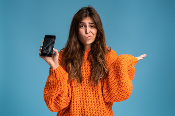 Long haired upset woman holding a out-of-use smartphone with broken screen and throw up hands in...