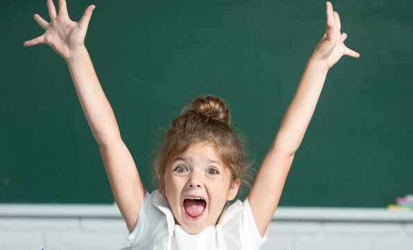 Excited school girl face with surprising expression against blackboard.