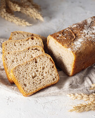 Fresh loaf of bread with several slices isolated on white background.Spikelets of rye on table