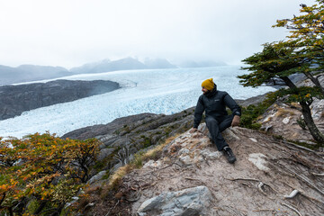 Obraz premium A young man sits on the rock with Grey Glacier on the background, Torres del Paine National Park, Chile