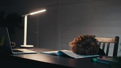 Distance learning, a boy sits at a table at home looking in a beech laptop. The concept of online education, home. Little boy doing homework at home late in evening.