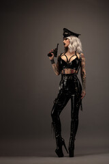 Pretty tattooed young woman wearing latex lingerie, cap and gun
