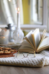 Naklejka na ściany i meble Plate of chocolate chip cookies, cinnamon sticks, soft blanket, open book and lit candles. Hygge at home. Selective focus.