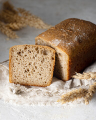 Loaf of sliced healthy bread and spikelets of wheat on linen kitchen towel on textured white board