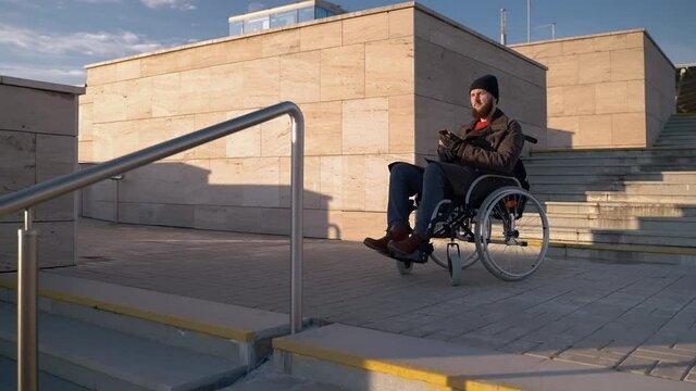 disabled man in wheelchair is standing in front stair in city, using map in app in smartphone