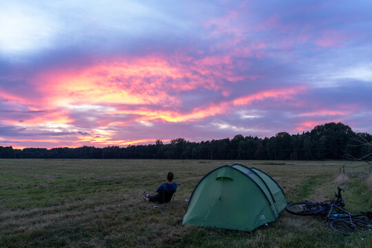 Person sitting in front of tent in field during a pink sunset, Grabow, Germany