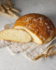 Loaf of round fresh homemade white bread with some slices cut isolated with wheat spikelets
