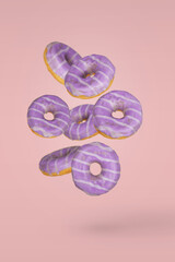 Purple decorated doughnuts in motion falling or flying on pink background.