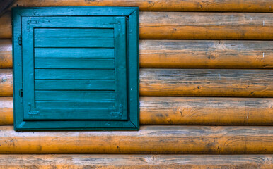 Close up of a wall of the house made of tree trunks with a blue wooden window
