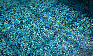 Bottom of an indoor pool with small blue tiles seen through the water, roof construction  shadow