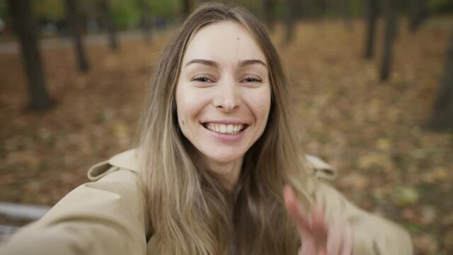 Caucasian woman taking selfie photo on smart phone outdoors in park while walking