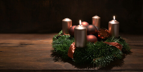 Second Advent wreath with copper colored candles and Christmas decoration baubles on a rustic wooden table against a dark brown background, panoramic format, copy space, selected focus