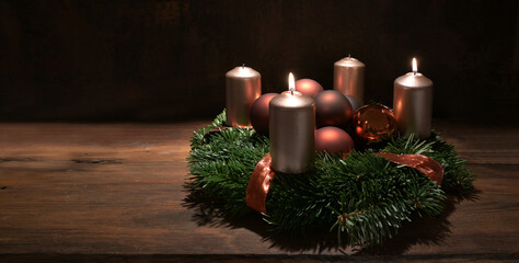 Second Advent wreath with copper colored candles and Christmas decoration baubles on a rustic wooden table against a dark brown background, panoramic format, copy space, selected focus
