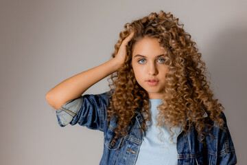 portrait of a cute smiling blonde girl with blue eyes and curly hair in a denim jacket. young woman with beautiful clean healthy skin. natural make up, spa concept, fashion concept. High quality photo