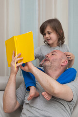 Father and son together enjoying reading and discussing school homework exercises from yellow textbook.