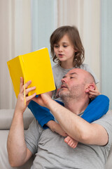 Father and son together enjoying reading and discussing school homework exercises from yellow textbook.