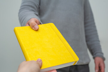 Close-up at male holding a yellow book in his hands.