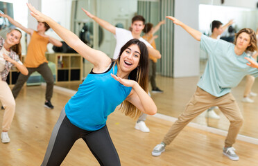 Naklejka na ściany i meble Happy brunette teenage girl dancer practicing active vigorous dance with group in modern studio.