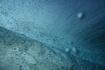underwater photo of a wave breaking in clear water and sunlight visible.