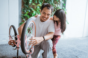 Young asian man with his daughter repairing child's bicycle wheel