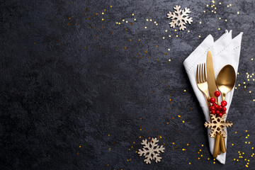 Christmas or new year table setting with golden cutlery on black stone table, card or menu template copy space flat lay