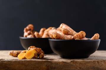 Fresh turmeric in a bowl on wooden with black background, Food ingredients in Asian food and used in beauty spa and herbal medicine