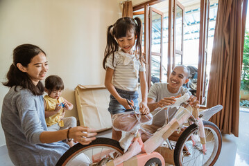 Happy daughter cutting plastic wrap while holding new mini bike