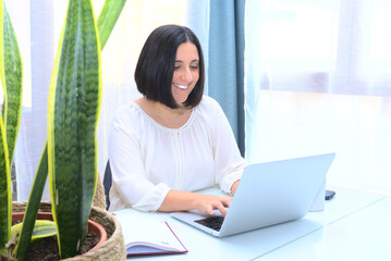 Happy office coworker smiles typing a report in laptop. White studio with plant