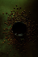 Coffee cup and coffee beans on black concrete surface. Flat lay with low-key and green tint.