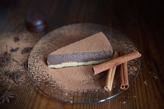 one piece of chocolate cheesecake on a plate decorated with cinnamon, candy and cloves on a wooden background. Close-up