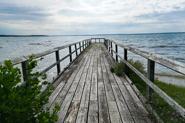 Obraz premium Old Weather Worn Dock--stretching out into a lake; front view of dock on overcast day with sun just starting to break through blue-grey clouds