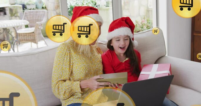 Animation of online shopping trolley icons over caucasian mother and daughter at christmas