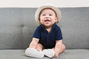 Adorable baby boy  first sitting on sofa. Cute infant Asian about 5-6 months old wearing blue...