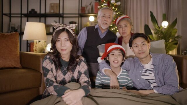 Asian family sits together watching TV on Christmas night. family, generation, christmas and people concept