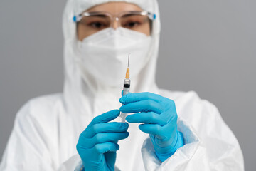 doctor in PPE suit holding syringe with Coronavirus (Covid-19) vaccine for injection test