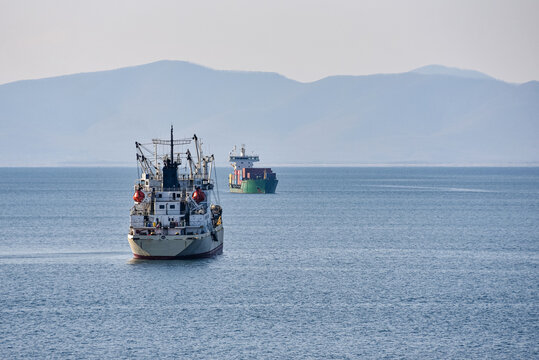 Two large ships at sea. A cargo ship and a fishing ship met at sea against the backdrop of a mountainous coastline