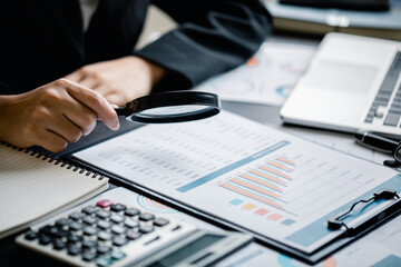 Close up of Businesswomen or Accountant using magnifying glass finding with analyzing business report graph and finance chart at the workplace, financial and investment concept.
