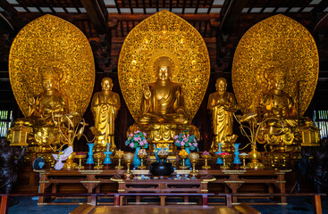 Golden sitting statues of Sakyamuni Buddha, Manjushri and Samantabhadra in Mahavira Hall in Baoshan or Treasure Mountain Serene Temple at Luodian Town, Baoshan, Shanghai, China.