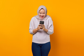 Portrait of cheerful attractive asian woman using mobile phone over yellow background