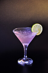 A glass of pale pink cocktail Cosmopolitan with ice and a slice of lemon on a black background.
