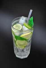 Tall glass of refreshing Mojito cocktail with ice, mint and lime on a black background.